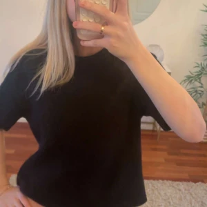 Svart kortärmad topp  - Enkel svart topp med korta ärmar och rund hals. Modellen är rak och något croppad, vilket ger en avslappnad vibe. Perfekt att matcha med jeans eller kjol för en clean look.