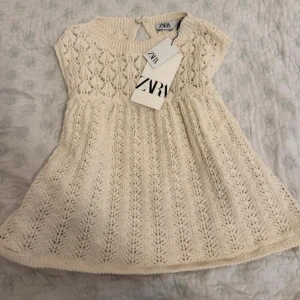 Vit stickad topp från Zara - Supersöt vit stickad topp  från Zara med kort ärm och rund hals. Klänningen har ett vackert hålmönster och knapp i nacken. Perfekt för dig som gillar romantisk stil. Mjuk och skön känsla tack vare det stickade materialet. Ny med prislapp - säljer för att jag köpt för liten storlek. 