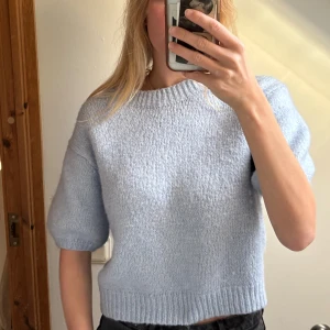 Ljusblå stickad croppad tröja - Supermysig ljusblå stickad tröja med kortare, croppad passform och halvkort ärm. Tröjan har ribbade muddar vid hals, ärmslut och nederkant. Perfekt att styla med jeans eller kjol för en chill look.