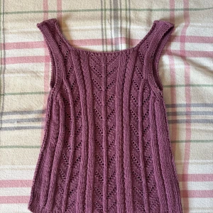 Stickad lila linnetopp med hålmönster - Säljer en stickad linnetopp i lila med snyggt hålmönster och breda axelband. Toppen har en rak och något loose passform, perfekt för dig som gillar en chill och unik look. Materialet är mjukt och skönt stickat, och färgen är en fin mörk lila ton.