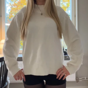 Vit stickad tröja med pärlor på - Supermysig vit stickad tröja med pärldetaljer på ärmarna. Den är perfekt för kyliga höst dagar men även enkel att matcha med allt.