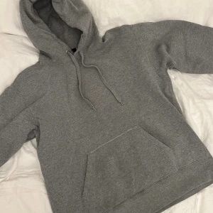 Grå hoodie från Paul & friends - Klassisk grå hoodie från Paul & friends i storlek M. Tröjan har huva med snörning, stor magficka och mjukt fleecefoder på insidan. Perfekt för chill dagar och enkel att matcha med jeans eller joggers. Köpt på NK!