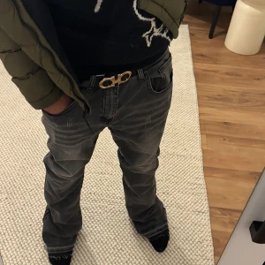 Svarta jeans med dragkedja nertill - Säljer ett par svarta jeans med slitningar och dragkedjor nertill på benen. Jeansen har en rak passform och är tillverkade i denim. Snyggt tvättade detaljer och klassisk femficksmodell. Perfekta för dig som gillar en avslappnad men trendig look.