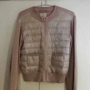 Beige quiltad jacka från Gina Tricot - Snygg rosa jacka från Gina Tricot med quiltad framsida och två fickor. Jackan har långärmade stickade partier och dragkedja framtill. Perfekt för dig som gillar en clean och chill look med lite extra detaljer.