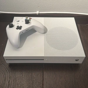 Xbox One S - Xbox One S i fint skick med original vit trådlös handkontroll. Konsolen har HDMI, USB och nätverksanslutningar. Inga synliga repor eller skador, fungerar utmärkt för gaming och streaming. Perfekt för både spel och underhållning.