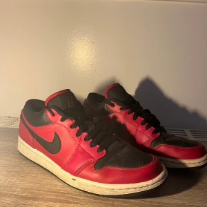 Nike Air Jordan 1 Low Bred Svart/Röd - Säljer ett par Nike Air Jordan 1 Low i den klassiska Bred-färgen. Skorna är i svart och rött skinn med svarta snören, perforerad tåbox och ikoniska Air Jordan-loggan broderad på hälen. Perfekt för dig som vill sticka ut med en tidlös sneaker.