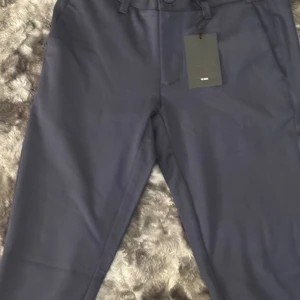 Mörkblå kostymbyxor från Only & Sons - Snygga mörkblå kostymbyxor från Only & Sons med klassisk rak passform. Byxorna har bälteshällor, knapp och dragkedja fram samt bakficka med knapp. Perfekta för en clean och stilren look. Materialet är mjukt och känns bekvämt mot huden.