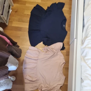 Volangtopp från Kappahl i rosa och marinblå - Två snygga volangtoppar från Kappahl i storlek 158/164. En är ljusrosa och den andra marinblå, båda med kort ärm och bred volang nertill samt puffiga volangärmar. Perfekt för dig som gillar en söt och trendig look. Tillverkade i mjuk bomull.Helt nya därefter priset ❤️