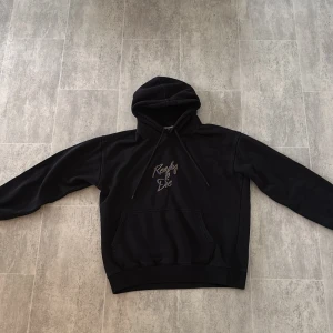 Svart Notorious B.I.G. hoodie M - Svart hoodie med huva och snörning från The Notorious B.I.G. På bröstet står det 'Ready to Die' i lila och guld, och på ryggen finns ett stort tryck med Notorious B.I.G. och Brooklyn-tryck. Klassisk känguruficka framtill.