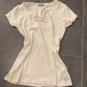 Vit ribbad topp - Säljer en vit ribbad topp från FB Sister i storlek S. Toppen har korta ärmar och snygg snörning vid halsen som ger en cool detalj. Materialet är mjukt och stretchigt, perfekt för dig som gillar enkel men stilren design.