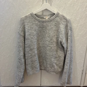 Grå stickad tröja från Gina Tricot - Mysig grå stickad tröja från Gina Tricot med rund hals och långärmad passform. Tröjan är tillverkad av en blandning av polyester, akryl, ull, alpaca och elastan vilket gör den både mjuk och varm. Perfekt för dig som gillar enkel och stilren look. Knappt använd!!