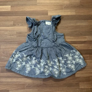 Jeansklänning med broderi - Supersöt blå jeansklänning från Newbie i storlek 56 (1-2mån). Använd fåtal gånger och är i nyskick. Volangärmar och knappar i ryggen. Bortklippt tvättråd.
