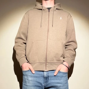 Beige zip hoodie från Ralph Lauren - Säljer en stilren beige hoodie från Ralph Lauren med dragkedja och broderad logga på bröstet. Jag är 190 cm lång och väger 86 kg pch den passar mig bra 😊 