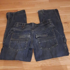 Mörkblå vintage jeans från Lab Industries - Säljer ett par mörkblå jeans från Lab Industries med snygga kontrastsömmar och coola bakfickor med lock. Jeansen har klassisk femficksdesign, breda hällor och är tillverkade i slitstarkt denim. Perfekta för dig som gillar en avslappnad och streetig stil.