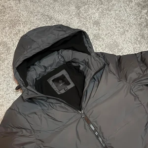 Mörkgrå Next vinterjacka  - Säljer en mörkgrå pufferjacka från Next i storlek S, med huva och dragkedja framtill. Jackan har två sidofickor med dragkedja och är perfekt för kyliga dagar. Enkel och stilren design som passar till det mesta.