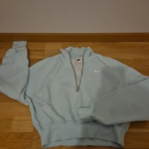 Ljusblå Nike half zip sweatshirt - Superfräsch ljusblå sweatshirt från Nike med half zip och klassisk vit swoosh på bröstet. Tröjan har lång ärm, ribbade muddar och en relaxed passform. Perfekt för chill dagar eller när du vill ha en sportig vibe.