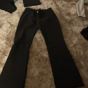 Svarta  kostymbyxor - Säljer ett par svarta kostymbyxor med lite utsvängt. Byxorna har en klassisk look med utsvängda ben och midja som sitter snyggt. Perfekta för dig som gillar stilrena och trendiga byxor. Materialet känns mjukt och följsamt.