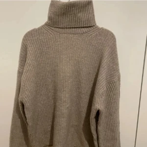 Beige ribbad polotröja från H&M - Säljer en beige ribbad polotröja från H&M i storlek S. Tröjan har en hög och bred polokrage, långärmade och loose passform. Materialet är stickat och känns mjukt och skönt mot huden. Perfekt för att hålla sig varm och snygg under kyliga dagar.
