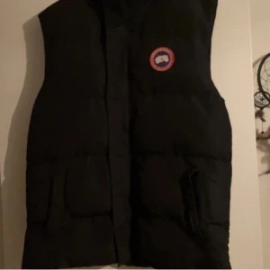 Svart dunväst från Canada Goose - Svart dunväst från Canada Goose med klassisk rund logotyp på bröstet, perfekt för kalla dagar. Säljer den då det inte är min stil längre. 