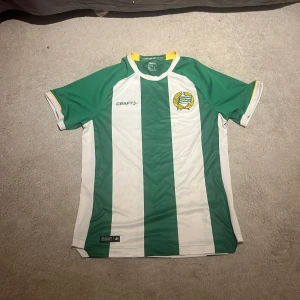 Hammarby fotbollströja Craft L - Säljer en officiell Hammarby fotbollströja från Craft i storlek L. Tröjan har breda gröna och vita vertikala ränder, klubbmärke på bröstet och gula detaljer vid krage och ärmslut. Tillverkad i lätt och funktionellt material, perfekt för match eller träning. Den är ifrån hammarbys cupsäsong 2024.Är oanvänd då den är för stor för mig.