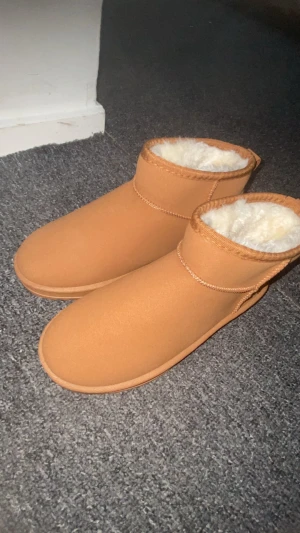 Bruna boots med fuskpälsfoder - Boots i ljusbrun färg med rund tå och platt sula. Insidan är fodrad med mjuk, vit fuskpäls som gör dem extra sköna och varma. Yttermaterialet är syntet och de har en enkel design utan snörning eller dragkedja. Perfekta för kalla dagar.