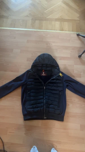 Mörkblå cardigan jacka från Parajumpers - Snygg mörkblå pufferjacka från Parajumpers med huva och hel dragkedja. Jackan har quiltad framsida och två sidofickor med dragkedja. Klassisk gul detalj vid kragen och ribbade muddar vid ärmslut. Perfekt för kyliga dagar.Ej använd jättemycket. Storlek M-L ‼️pris ej hugget i sten ‼️