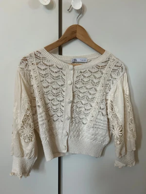 Vit spetskofta från Zara, storlek S - Superfin vit kofta från Zara med spetsdetaljer och stickat mönster. Koftan har rund hals, knappar framtill och långa ärmar med vackert broderade och virkade partier. 