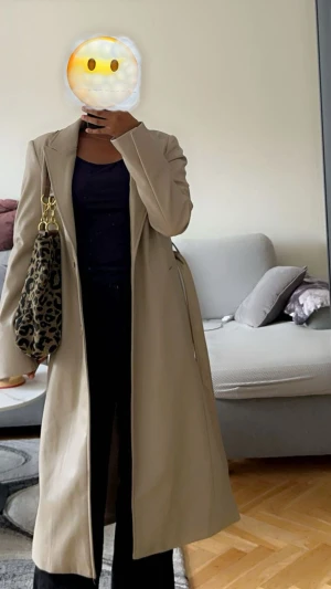 Beige lång kappa från Amisu - Snygg beige kappa från Amisu med klassisk krage och knappar framtill. Lång modell med rak passform och helfodrad insida. Perfekt för dig som gillar stilrena och minimalistiska plagg. Passar till både jeans och dressade outfits.