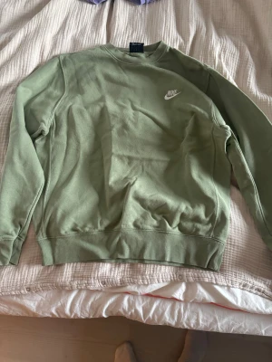 Grön sweatshirt från Nike - Snygg grön sweatshirt från Nike med klassisk logga i vitt på bröstet. Tröjan har rund hals, långa ärmar och ribbade muddar vid ärmslut och nederkant. Perfekt för chill dagar eller när du vill ha en enkel och stilren look.