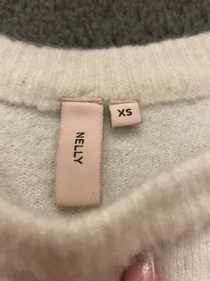 Vit croppad stickad tröja Nelly XS - Supermjuk och croppad vit stickad tröja från Nelly i storlek XS. Tröjan har rund halsringning och långa ärmar, perfekt för lager-på-lager och chill vibes. Enkel och stilren design som är lätt att matcha med jeans eller kjol. 