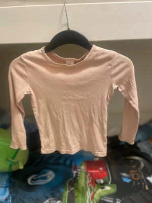 Ljusrosa långarmad tröja Lindex - Söt ljusrosa långarmad tröja från Lindex Kids i storlek 122. Tröjan har en enkel design med rund hals och dekorativ kant med små volanger. Mjuk och skön bomull som passar perfekt till skolan eller häng med kompisar. Barn till tjejer 
