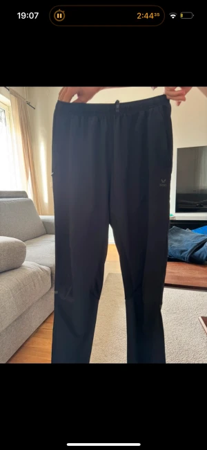 Svarta träningsbyxor från SOC - Svarta träningsbyxor från SOC med elastisk midja och raka ben. Byxorna har diskreta fickor på sidorna och är tillverkade i ett lätt och smidigt syntetmaterial som passar perfekt för träning eller chill. Enkel och stilren design.