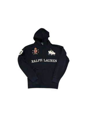 Mörkblå hoodie Polo Ralph Lauren - Mörkblå hoodie från Polo Ralph Lauren i junior storlek XL, vilket motsvarar runt S-M. Riktigt snygg hoodie med stor vit logga och text framtill, broderad patch på bröstet och siffra 3 på ryggen. Finns lite tecken på användning. Skriv vid vidare funderingar!