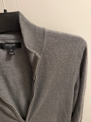 Grå Matinique kofta   - Snygg grå kofta från Matinique i storlek S. Tröjan har en ribbad krage, hel dragkedja framtill och långa ärmar. Materialet är mjukt och känns som bomull eller en bomullsblandning. Perfekt för lager-på-lager och chill stil.