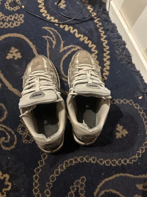 Nike silverfärgade sneakers - Nike sneakers i silver med mesh och syntetpaneler, klassisk swoosh på sidan och snörning framtill. Modellen har en chunky platt sula och rund tå. Perfekt för dig som gillar sportig stil och metallic vibes.