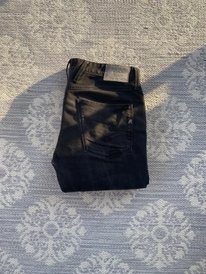 Svarta Replay jeans herr, storlek 33/34 - Säljer ett par svarta Replay jeans i klassisk modell med raka ben och snygga detaljer på bakfickan. Jeansen har normal passform och är tillverkade i mjukt denimtyg. Perfekta för dig som gillar stilrena och tidlösa jeans.