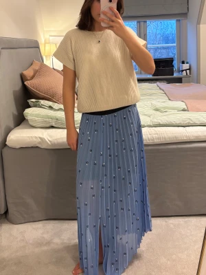 Maje kjol - En ljusblå plisserad långkjol med små svarta och vita hjärtmönster. Kjolen har en skön loose passform och ett svart midjeband. Materialet känns lätt och flowy och har en slits framtill.