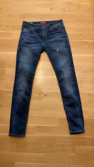 Jack & Jones Skinny Liam jeans blå - Snygga mörkblå skinny jeans från Jack & Jones, modell Liam. Klassisk femficksdesign med smal passform och orangea kontrastsömmar. Jeansen är tillverkade i stretchig denim för extra komfort och har en modern tvättad look.