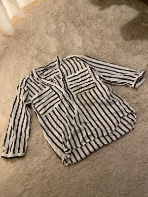 Randig skjorta - Snygg vit svart randig skjorta, från Vero Moda i storlek XS. Skjortan har två stora bröstfickor, knappar framtill och som slutar på mitten. Materialet är mjukt och fuktigt och skjortan har korta ärmar med små knappar💞