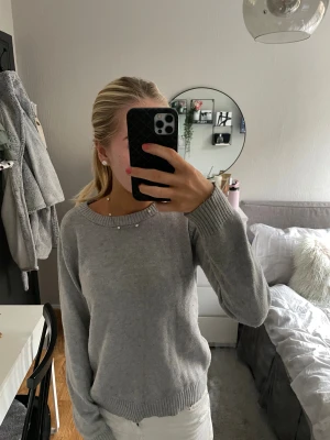 Ljusgrå stickad tröja - Superfin ljusgrå stickad tröja med rund halsringning Tröjan har långa ärmar och breda ribbade muddar vid ärmslut och nederkant. Perfekt för lager-på-lager och enkel att matcha med allt.