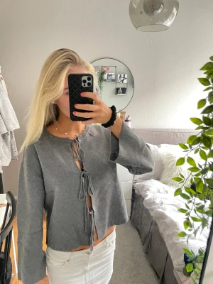 Grå knytblus med vida ärmar - OBS‼️ jättesnygg att ha bak o fram så den är öppen i rygg!! Säljer en grå blus med tre knytningar framtill och vida ärmar. Toppen är croppad och har en rak passform. Perfekt för dig som gillar en chill och trendig look. Materialet känns mjukt och toppen är enkel att styla med både jeans och kjol. 