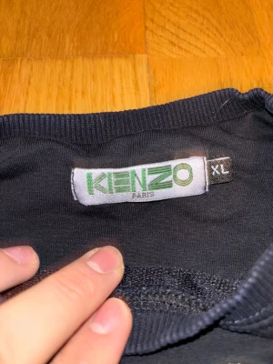 Svart Kenzo tröja med tigerbroderi som har krympt  - Kenzo crewneck i svart med ikoniskt tigerbroderi i blått, gult och grönt på bröstet. Tröjan har ribbade muddar vid ärmslut och nederkant, samt rund hals. Perfekt statement-plagg för dig som gillar streetwear och snygga detaljer.