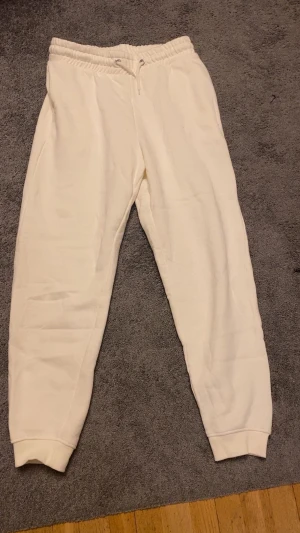 Vita mjukisbyxor med snörning - Snygga vita mjukisbyxor med elastisk midja och snörning framtill. Byxorna har ribbade muddar vid bensluten och är tillverkade i mjukt bomullsmaterial. Perfekta för chill dagar eller när du vill vara extra bekväm.