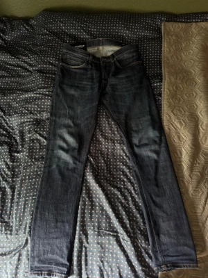 Dondup mörkblå skinny jeans herr - Snygga mörkblå jeans från Dondup, modell George Skinny Fit. Klassisk femficksdesign med kontrastsömmar och smal passform. Tillverkade i slitstarkt jeanstyg med italiensk kvalitet. Perfekt för dig som gillar en modern och stilren look.