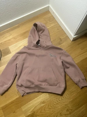 Rosa hoodie med New York-tryck - Snygg rosa hoodie med huva och magficka, perfekt för chill dagar. Tryck med 'New York' på bröstet ger en cool vibe. Mjuk och skön, med ribbade muddar vid ärmar och nederkant. Passar dig som gillar enkel och stilren streetwear.