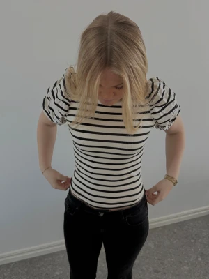 Snygg topp - Säljer en snygg topp med svarta och vita ränder och puffiga korta ärmar. Toppen har rund halsringning och är figurnära i modellen. Materialet är mjuk bomull som känns skönt mot huden. Perfekt för dig som gillar en trendig och stilren look.