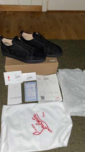  Christian Louboutin - Säljer ett par svarta sneakers från Christian Louboutin i mocka med klassisk röd sula och rund tå. Skorna har snörning och kommer med originalkartong, dustbag och äkthetsbevis. Perfekt för dig som gillar exklusiva och stilrena sneakers med lyxig vibe.