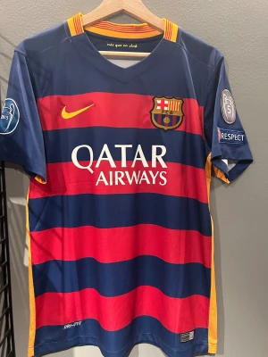 FC Barcelona Messi 10 matchtröja - Säljer en officiell FC Barcelona fotbollströja med Messi 10 på ryggen. Tröjan är randig i mörkblått och rött med gula detaljer, klubbmärke på bröstet och Champions League-patch på ärmen. Materialet är lätt polyester med Dri-FIT-teknologi för bästa komfort. Helt ny med tagg en replika