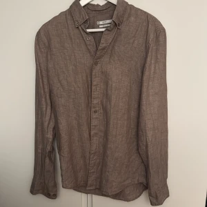 Brun linneskjorta från C, regular fit - Säljer en brun långärmad skjorta i 100% linne från C. Skjortan har klassisk krage med knappar och regular fit, perfekt för en chill och stilren look. Enkel design utan mönster, passar dig som gillar naturliga material och avslappnad stil.