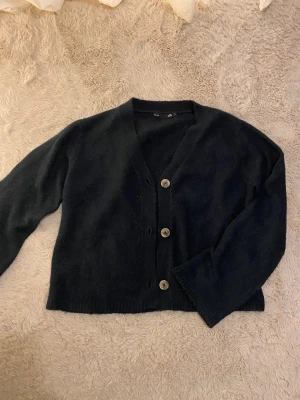 Mörkblå kofta med knappar - Mysig mörkblå kofta från Lager157 med v-ringning och tre stora, ljusa knappar framtill.Koftan är i S men passar som XS också. Koftan är stickad och har långa ärmar samt ribbade muddar vid ärmslut och nederkant. Inte använt den så ofta💞